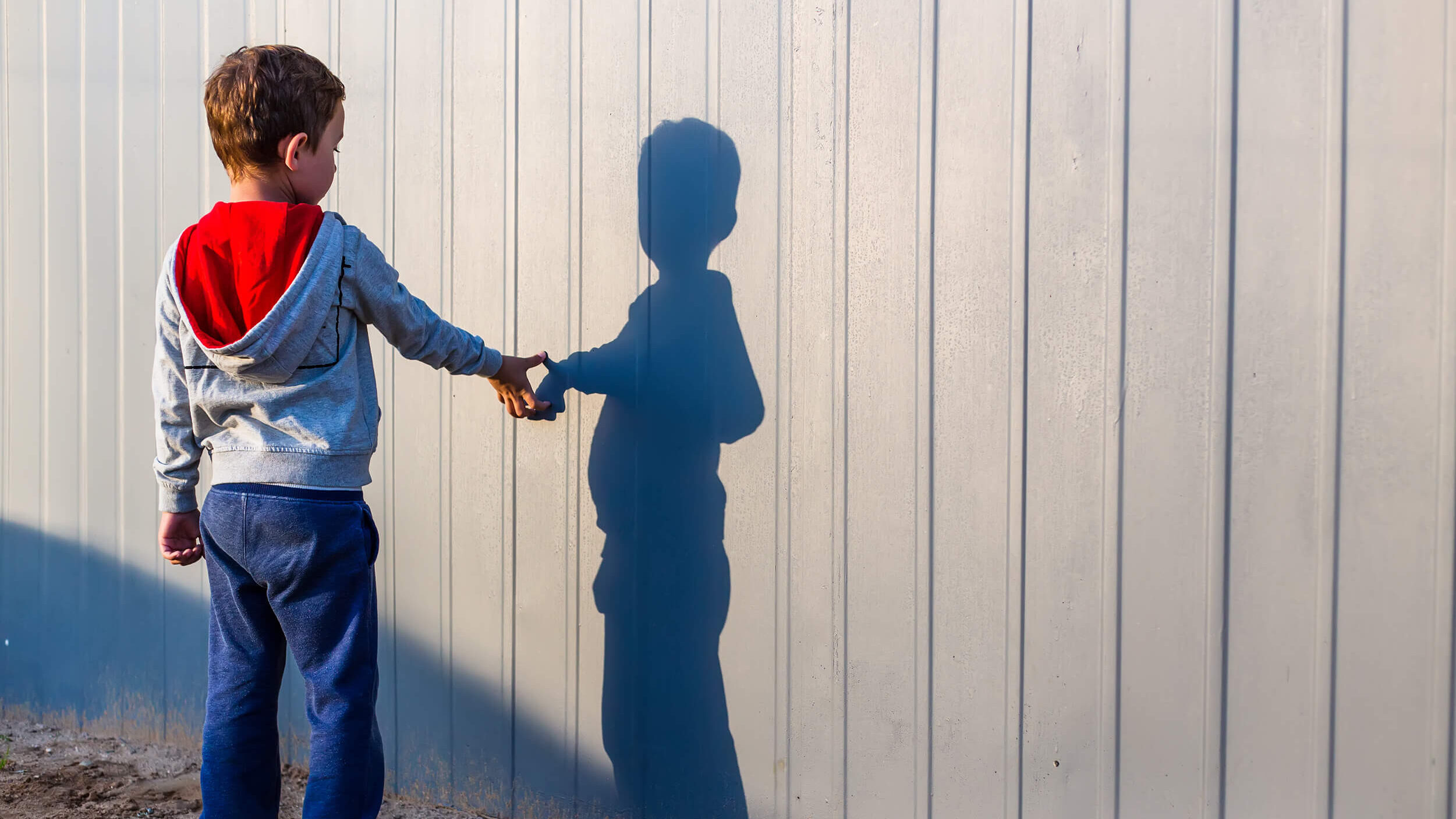 A young boy reaches out to touch his shadow on a wall.